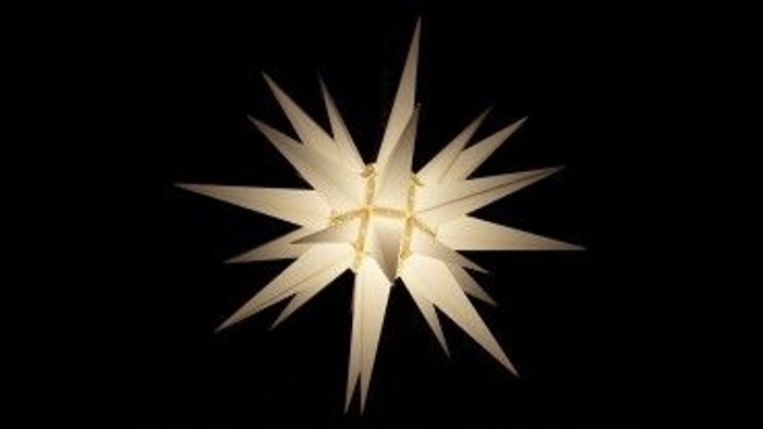 Ein weißer, sternförmiger Weihnachtsdekoration vor schwarzem Hintergrund.