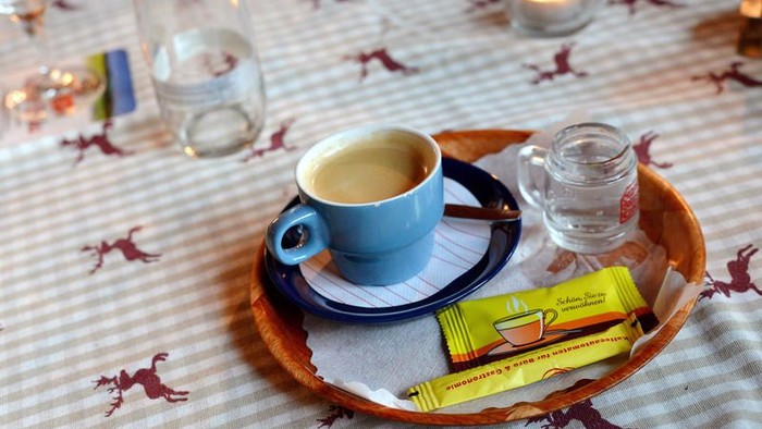 Ein Holztablett mit Kaffeetasse, Untertasse, Zucker und einem kleinen Glas auf einem Tisch mit Pferde-Muster.