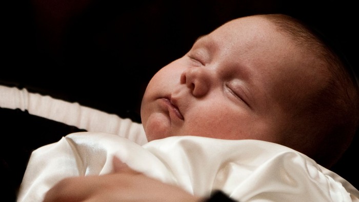 En baby sover fredeligt, indsvøbt i et hvidt tæppe.