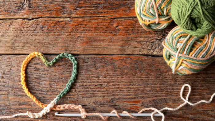 Håndlavet hjerte i hækling på træbord med farverigt garn og hækle kroge i nærheden.