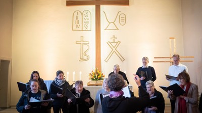 Eine Gruppe von Menschen, die in einem Kirchenchor singt und einem Altar mit symbolischen religiösen Verzierungen zugewandt ist.