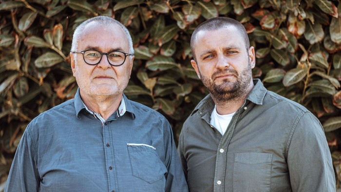 To old mænd står sammen foran en busk.