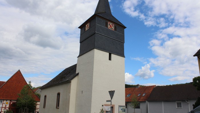 Weiße Kirche mit schwarzem Dach und Uhrturm vor blauem Himmel.