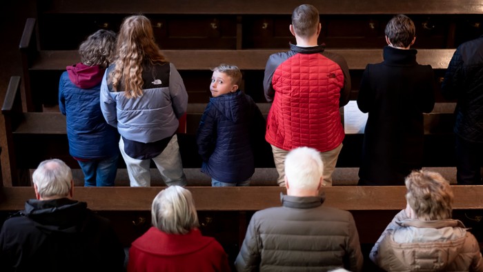 Menschen stehend in den Bankreihen der Friedenskirche Offenbach. Sie sind von hinten von der Empore aus fotografiert. Nur ein Junge dreht sich zum Fotografen um