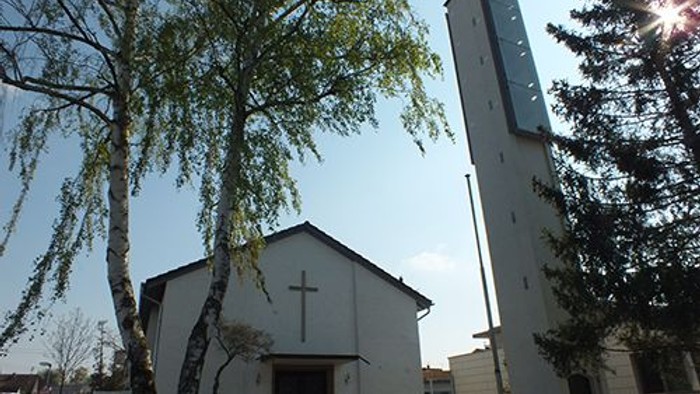 Weiße Kirche mit hohem Turm und Kreuz vor Baum