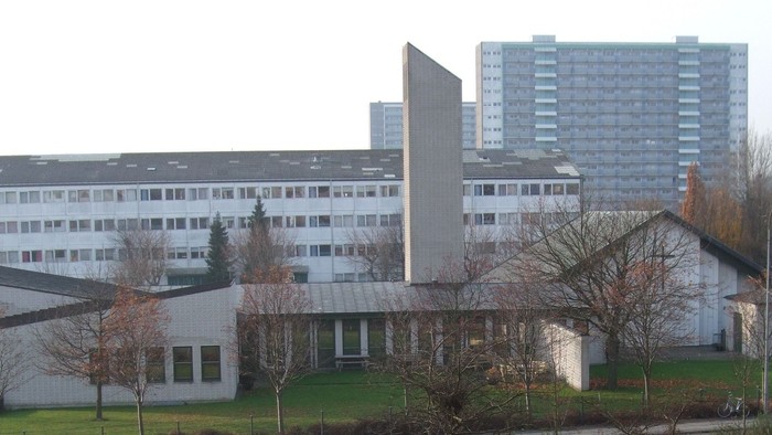 Moderne institutionsbygninger med et højt boligkompleks og løvfrie træer om vinteren.