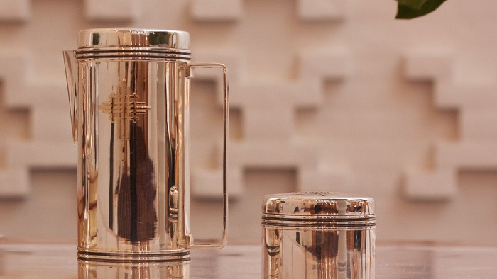 En stor og en lille guldfarvet kaffekanner og sukkerskål på bord.