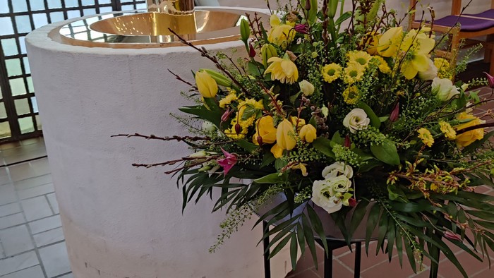 En stor blomsterarrangement med gule og hvide blomster står på en stativ foran en fontæne.