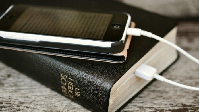 Bibel, die mit einem Kabel mit einem Smartphone verbunden ist