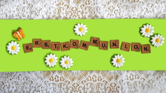 Ein grüner Streifen mit Buchstaben und Gänseblümchen darauf, auf weißer Spitze.