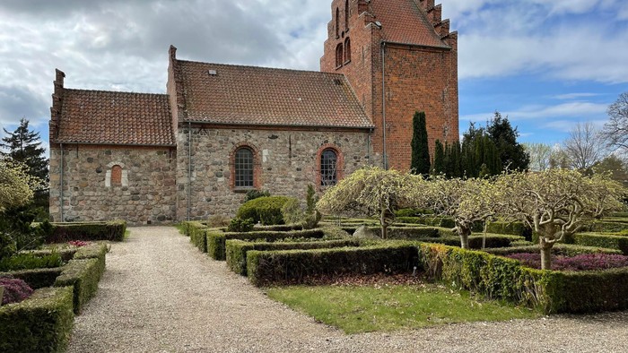 Historisk stenbygning med rødt tegltag og velplejet have.