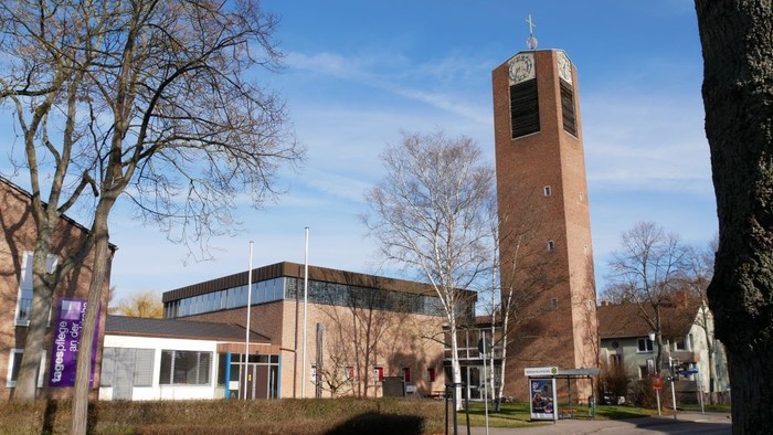 Modernes Gebäude mit hohem Uhrturm und umgebenden Bäumen.