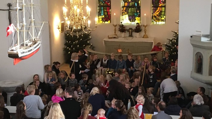 En folkemængde i kirke med juletree og skibsmodel.