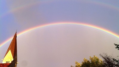 Regnbuen spænder over kirke med tårn.