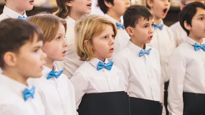 En gruppe børn synger i kor, alle med blå boller og hvide skjorter.