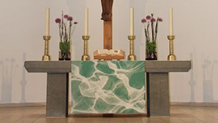 Das Bild zeigt einen Altar in einer Kirche mit einem Kruzifix und Kerzen.