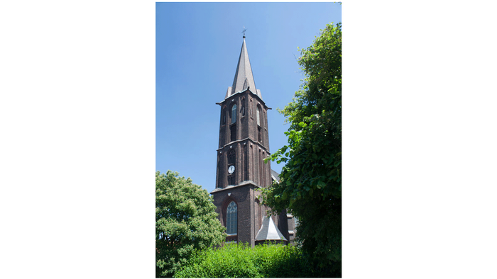 Hoher Uhrturm, umgeben von Bäumen unter einem klaren blauen Himmel.