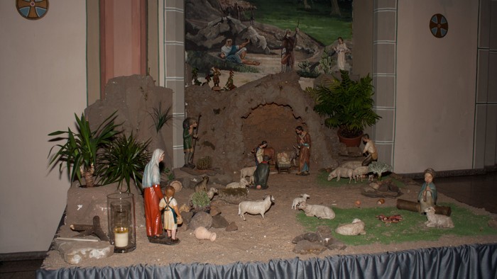 Eine Krippe mit verschiedenen Figuren und Tieren, darunter eine Familie und Schafe, ist auf einem Tisch aufgebaut.