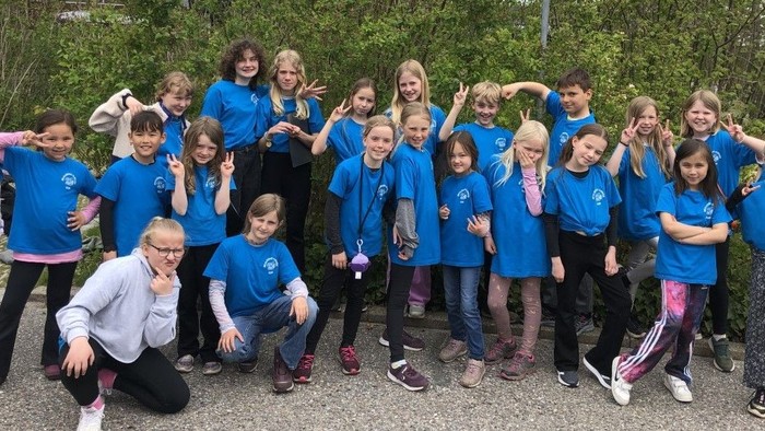 En gruppe børn i blå T-shirts poserer sammen udendørs