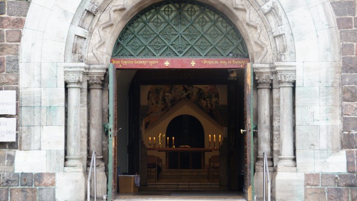 Der Eingang zu einer Kirche mit einem grünen Vordach und Kerzen im Inneren