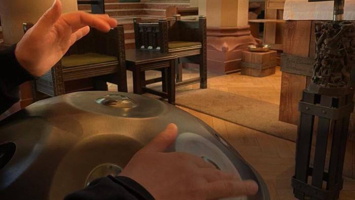 Person spielt auf einem Metallobjekt, Raum mit Möbeln und Dekorationen