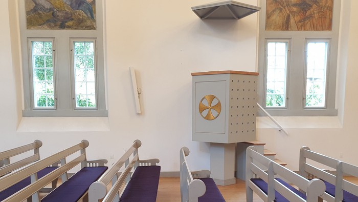 En lille kapel med bænke, pulpet og to billeder på væggen
