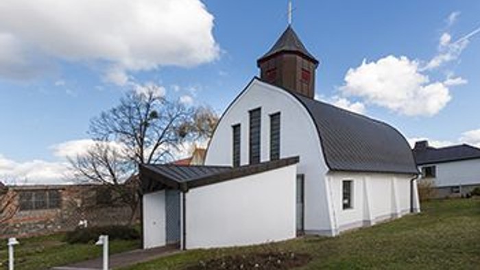Weißes Gebäude mit schwarzem Dach und Turm auf grüner Wiese