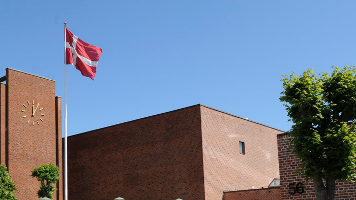 En rød hvid flag på et mørkt teglmurstensbygning med klokke.