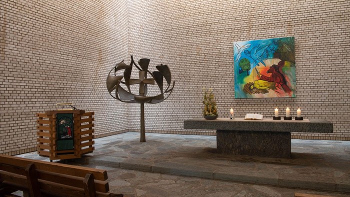 Ein moderner Raum mit einer Metallskulptur, einem Bild an der Wand und einem Altar mit Kerzen.