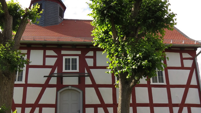 Das Bild zeigt ein traditionelles deutsches Fachwerkhaus mit einem spitzen Dach und einem Wetterhahn.