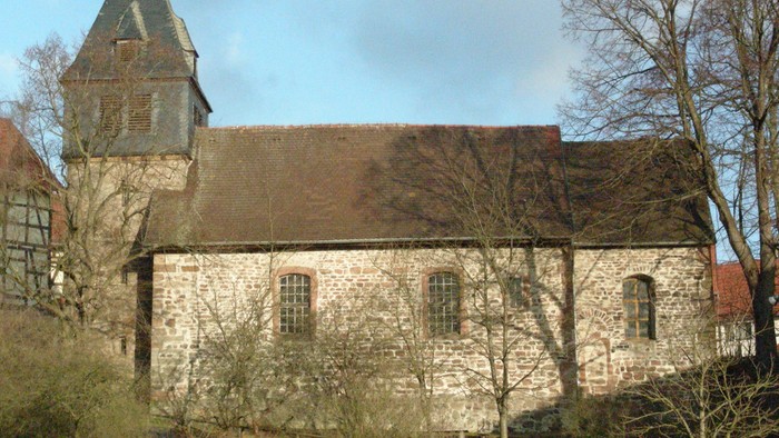 Alte Kirche mit Turm und spitzem Dach, umgeben von Bäumen und Büschen
