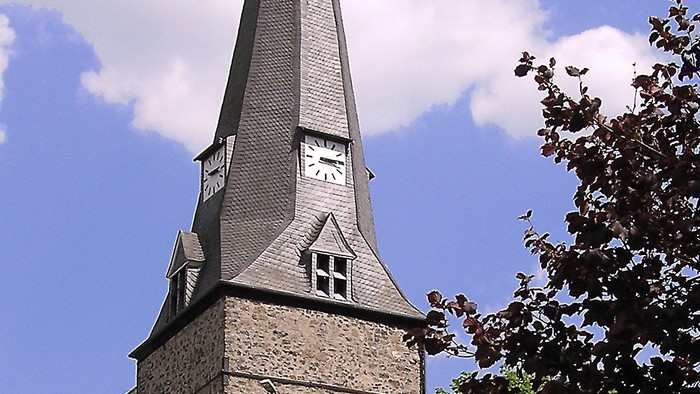 Ein hoher Kirchturm ragt in den klaren blauen Himmel.