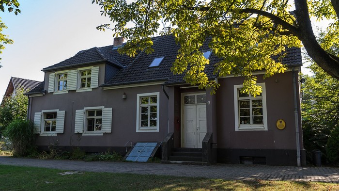 Haus mit grauer Fassade und grünen Fensterläden unter Bäumen.