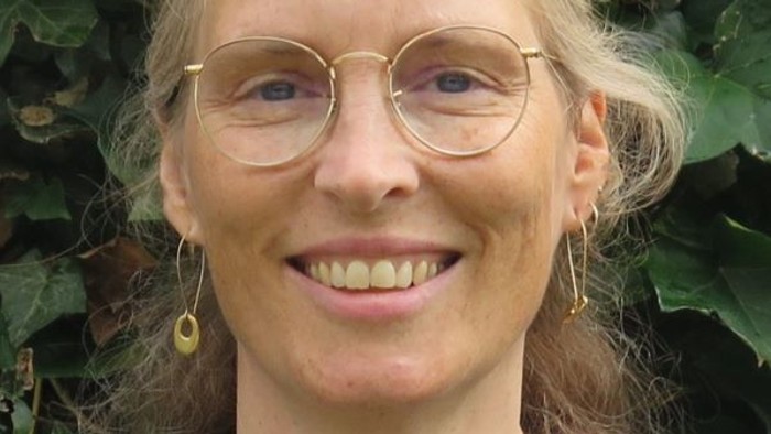 Kvinde med briller og øreringe, der smiler udendørs.