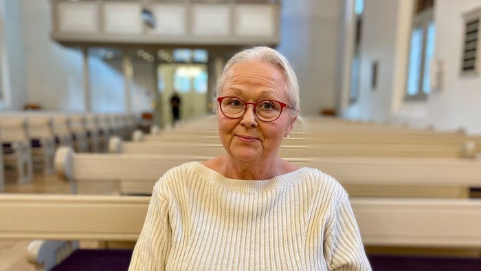 En kvinde står i en kirke med håndene sammen.