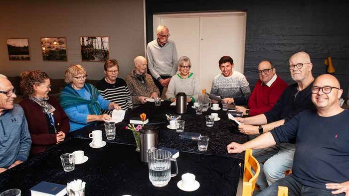 En gruppe af mennesker sidder sammen ved et bord med kaffe og te.
