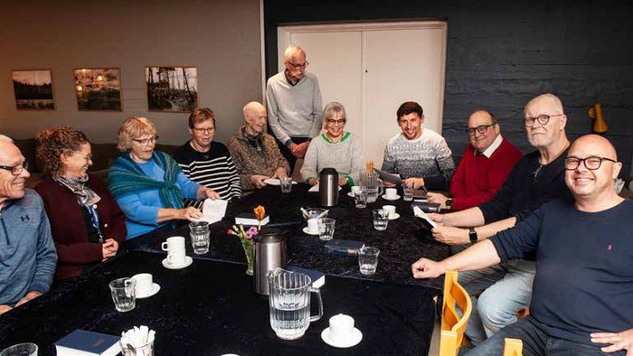 En gruppe af mennesker sidder sammen ved et bord med kaffe og te.