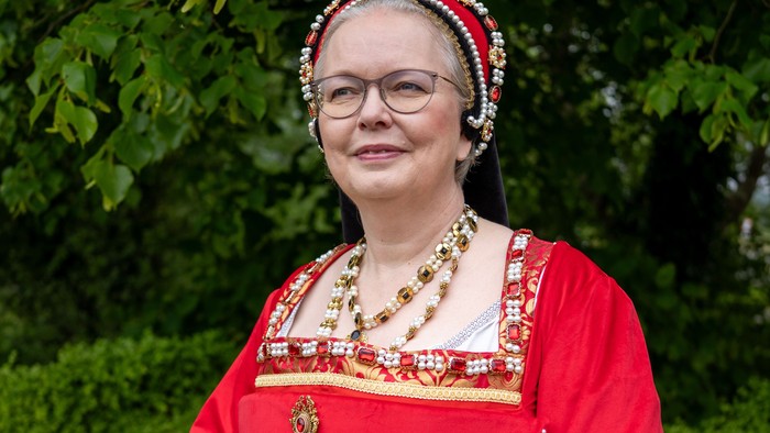 Kvinde i rød historisk kjole med guldkanter og hvide handsker.