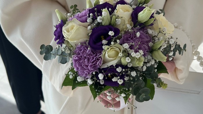 En kvinde i hvidt tøj holder en blomstertæppe med lilla og hvide blomster.