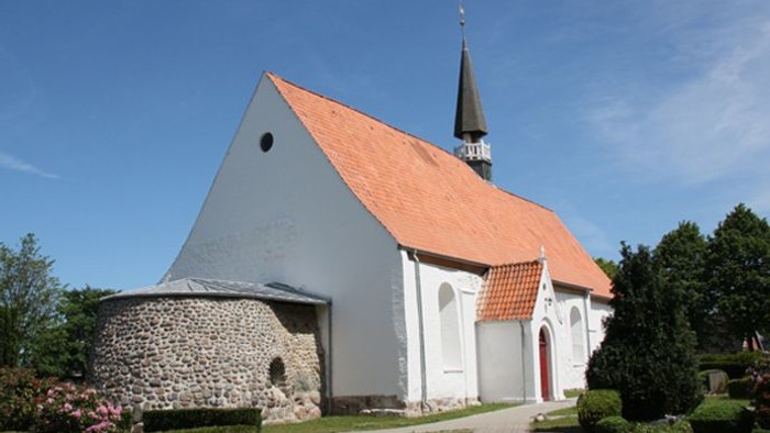 Kleine Kirche mit rotem Dach und Turm, umgeben von Grün.