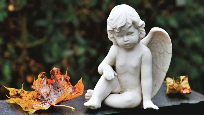 En lille engelstatue sidder på en steen med høstblade.