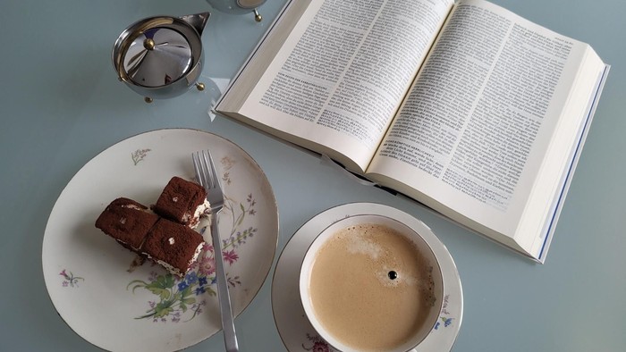 Ein Buch, eine Teetasse, eine Teekanne und ein Teller mit Kuchen auf einem blauen Tisch