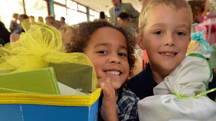 Zwei Kinder mit Geschenken umarmen sich und lächeln.