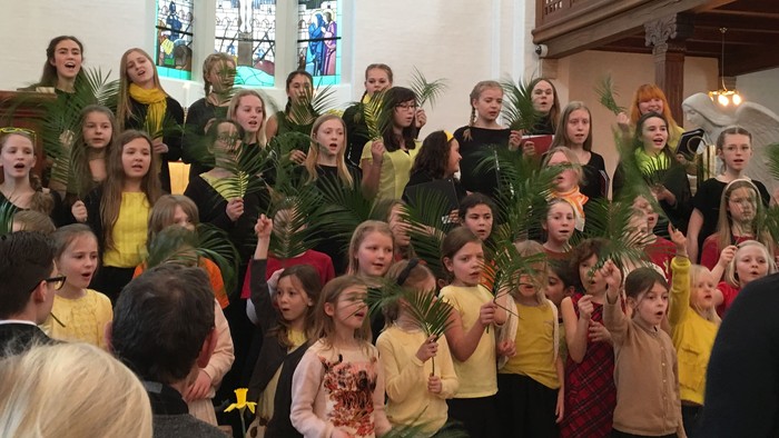 En gruppe børn i farverige klæder holder palmeblade i en kirke.
