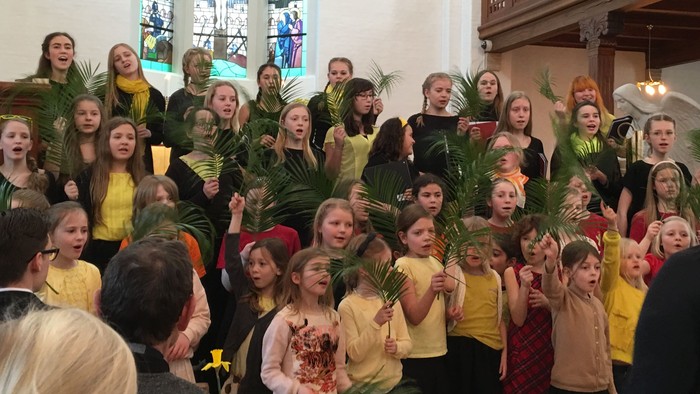 En gruppe børn i farverige klæder holder palmeblade i en kirke.