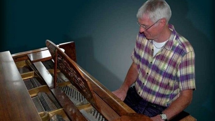 En mand undersøger det indre mekanisme i et åbent klaver, mens han har en ternet skjorte på.