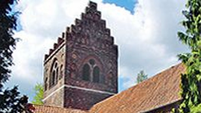 Et gammelt teglsteinshus med en tårnagtig struktur og bægerformede vinduer.