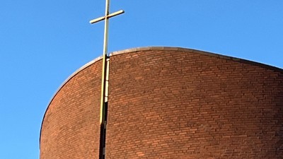 En stor mørk murstenskirke med et guldæret kors på toppen.