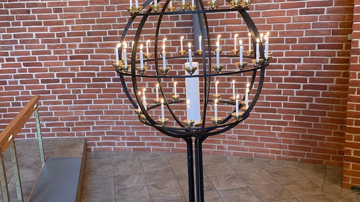En stor kandelaber med mange lys på et podie foran mur af røde teglsten.