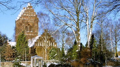 En snedækket park med en højtårnet kirke i baggrunden